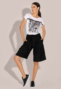White T-shirt with a black zebra stripe design, paired with loose black shorts featuring a tied waist, and black sneakers with white soles.