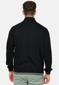 Svart zip-up jakke med høy krage, ribbestrikkede mansjetter og kant med hvite striper. Glatt stoff med en avslappet passform.