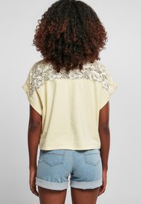 Kortärmad gul topp med spetsdetaljer på baksidan, kombinerad med ljusblå denimshorts med uppvikta fållar och två bakfickor.