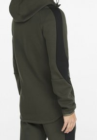 Olijfgroene hoodie met een zwart zijpaneel, voorzien van een trekkoord in de capuchon, een gladde textuur en een getailleerde pasvorm. Verstelbare mouwen, geen zichtbare branding.