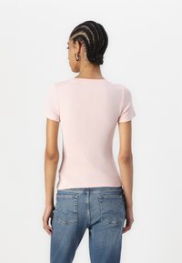 T-shirt en coton côtelé rose avec un col rond et des manches courtes, associé à un jean en denim bleu, montrant des détails à l'arrière.