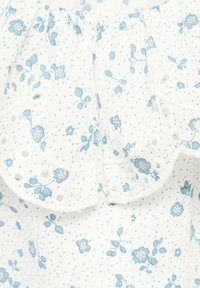 Tessuto bianco con un delicato motivo floreale blu, caratterizzato da un bordo in pizzo ad occhio e da sottili pois. Texture morbida e leggera.