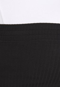 Gros plan sur une taille en tissu noir à rayures au-dessus d'un tissu blanc à rayures, montrant les détails de texture et de couture.