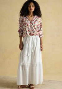 Bluzka w kwiaty z guzikami z przodu i elastycznymi mankietami, zestawiona z białą, warstwową maxi spódnicą z ociepleniami i akcentami w postaci frędzli.