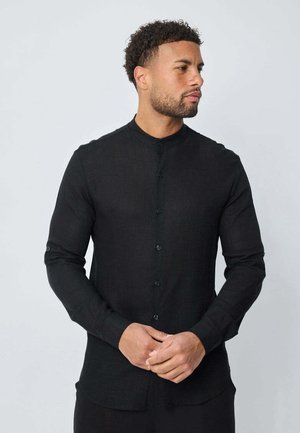 Chemise noire à manches longues avec col mandarin, comportant des boutons sur le devant, coupe ajustée et tissu texturé. Idéale pour une tenue décontractée.