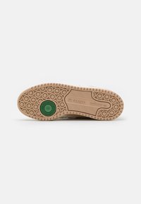 Adidas tenisica s potplatima, smeđi gumeni potplat s kružnim uzorkom. Ima zeleni kružni naglasak i oznake za identifikaciju brenda.