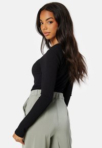 Top lungo a maniche nere a coste abbinato a pantaloni verdi chiaro a vita alta. Il tessuto appare liscio e aderente, con dettagli di texture sottili.