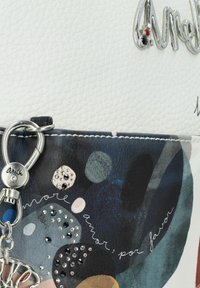 Weiße strukturierte Oberfläche mit einem mehrfarbigen Punktdesign und Verzierungen. Ausgestattet mit einem silbernen Hardware-Verschluss und dem "Anitk"-Logo. Dekorative Handschrift.