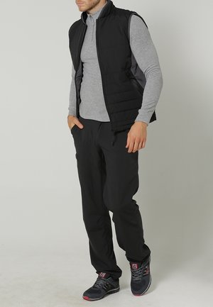 Svart vadderad väst över en grå långärmad tröja, kombinerad med svarta byxor och grå sneakers med rosa detaljer.