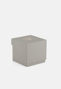 Scatola grigia con texture e un logo triangolare dorato sulla parte superiore. Presenta un coperchio e una forma semplice e geometrica.