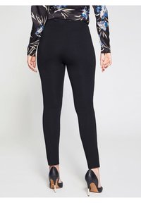 Černé legíny s přiléhavým střihem, vyrobené z elastické látky, končící u kotníků, spárované s černými vysokými podpatky.