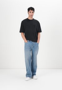 Schwarzes Baumwoll-T-Shirt mit kurzen Ärmeln und einem kleinen Logo. Hellblaue Jeans mit lockerer Passform. Weiße Sneakers runden das Outfit ab.