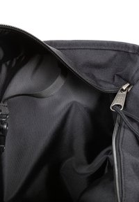 Zwarte stoffen tas binnenkant met een gladde textuur, ritssluiting en een metalen ritstrekknoop. Beschikt over een lus voor het bevestigen van een hengsel aan de binnenkant.