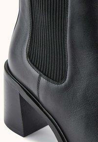Botte de cheville en cuir noir avec des panneaux élastiques texturés sur les côtés, un talon bloc et un design élégant axé sur une silhouette moderne.