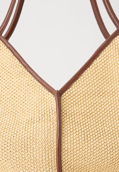 Gros plan d'un sac beige tissé avec garniture et poignées en cuir marron sur un fond clair.