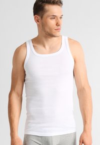 White ribbed tank top made from breathable cotton. Features wide straps and a square neckline, designed for comfort and ease of movement.