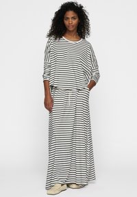 Conjunto de top a rayas y falda maxi en crema con rayas horizontales negras; ajuste holgado, tejido suave, cintura con cordón, combinado con calzado ligero.