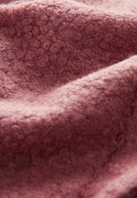 Tissu textile en rose doux avec une surface texturée présentant de petites boucles surélevées, créant une apparence chaleureuse et une sensation tactile agréable.