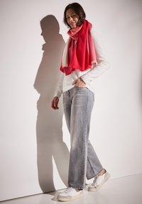 Un pull blanc, un jean large gris et une écharpe à dégradé rouge. Des baskets blanches avec des accents gris. Textures douces et ombres légères.