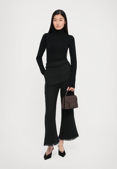 Must värvitud turtleneck, tekstuuriga mustad flared püksid, mille alumine äär on kulunud, ja pruun käekott, millel on reljeefne logo. Mustad terava ninaotsaga kontsad lõpetavad välimuse.