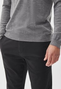 Pulover gri tricotat cu guler rotund, având tiv și manșete ribbate, asortat cu pantaloni negri drepți. Textură fină, fără modele vizibile.