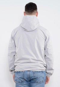 Giacca con cappuccio grigia chiara realizzata in un materiale leggero e liscio. Presenta polsini elasticizzati e un design semplice senza chiusure visibili.