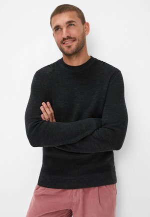 Zwart gebreid trui met een ronde hals en geribbelde manchetten, gedragen met lichtroze corduroy broek. De stof lijkt gestructureerd en warm.