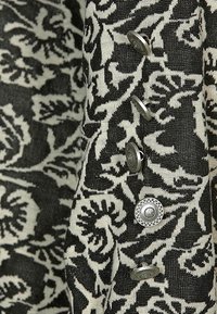 Svartvitt blommönstrad tyg med silverknappar på sidan. Texturen ser vävd ut med en slät yta.