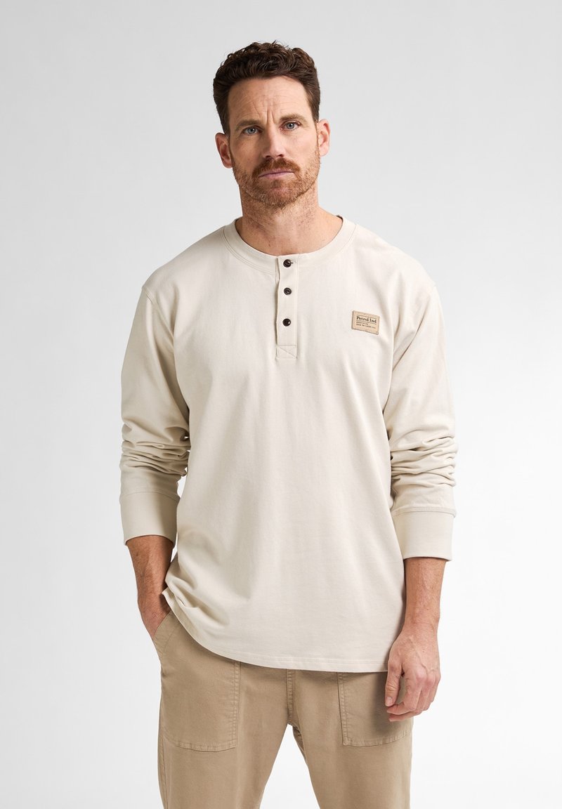Beige langslavige henley shirt met vier donkere knopen, voorzien van een klein patchlogo op de linkerborst en geribbelde manchetten.