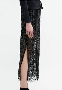 Black lace skirt with side slits and intricate floral patterns, featuring a sheer texture and a scalloped hem. Worn with a fitted top.