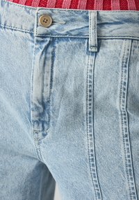 Lyse blå denimjeans med standard knappelukk og subtile slitasjedetaljer, samt ton-i-ton sømmer langs sømmene.