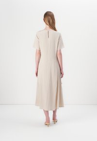 Beige midi-kjole med korte ermer, teksturert stoff, nøkkelhullsdetalj bak, og en tettsittende midje som vidder seg forsiktig mot kanten.