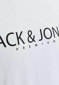 T-shirt en coton blanc avec un texte noir en gras "JACK & JONES PREMIUM", avec une texture lisse et un col rond.