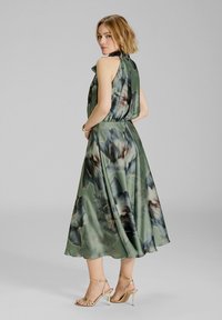 Abito lungo e fluente verde con un motivo floreale in tonalità scure. Tessuto morbido e leggero con vita adattata e design senza maniche.