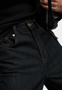 Donkerblauwe denim jeans met een gladde textuur, voorzien van goudkleurige accenten, contrasterende stiksels en een klassieke vijf-pocketontwerp.