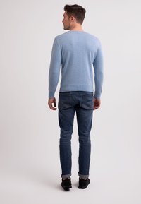 Ljusblå tröja i en mjuk, stickad struktur, kombinerad med mörkblå jeans. Outfitten har en avslappnad passform, med uppvikta ärmar och svarta skor.