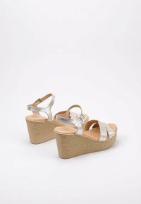Sandalias de cuña metálicas plateadas con parte superior texturizada, tira de tobillo ajustable y suela de plataforma de mimbre marrón. Presenta un diseño de tiras cruzadas.