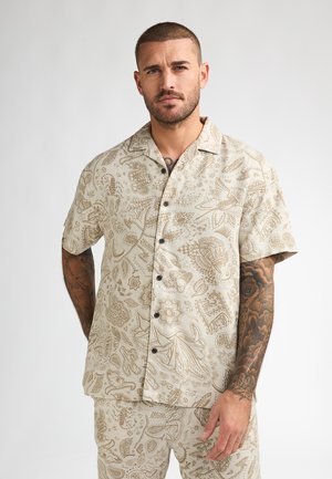 Beige shirt met korte mouwen en ingewikkelde bruine patronen, met kraag, knoopsluiting aan de voorkant en een losse pasvorm. Bijpassende broek kan aanwezig zijn.