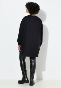 Vestito felpa nero oversized con maniche lunghe, scollatura tonda e polsini a coste. Abbinato a leggings neri lucidi e stivaletti con borchie.