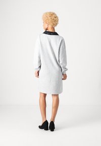 Vestido cinza de sweatshirt com mangas longas e gola preta, apresentando um corte descontraído e uma textura suave. Sapatos de salto alto pretos.