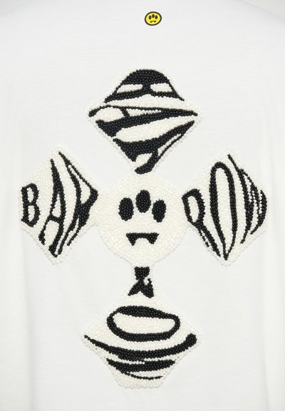 Λευκό μπλουζάκι με υφή που εμφανίζει μια μαύρη και λευκή σχεδίαση από χάντρες σε διάφορα σχήματα και μοτίβα, συμπεριλαμβανομένου ενός κεντρικού μοτίβου πατούσας.