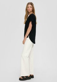 Top negro de manga corta con un corte holgado, combinado con pantalones blancos de pierna ancha y sandalias de plataforma negras. Diseño sencillo, apariencia casual.