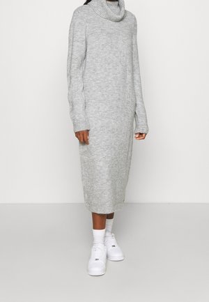 Graues, gestricktes Rollkragenkleid mit langen Ärmeln, gerippten Bündchen und Saum; getragen mit weißen Sneakers, in Knielänge. Glatte Textur.