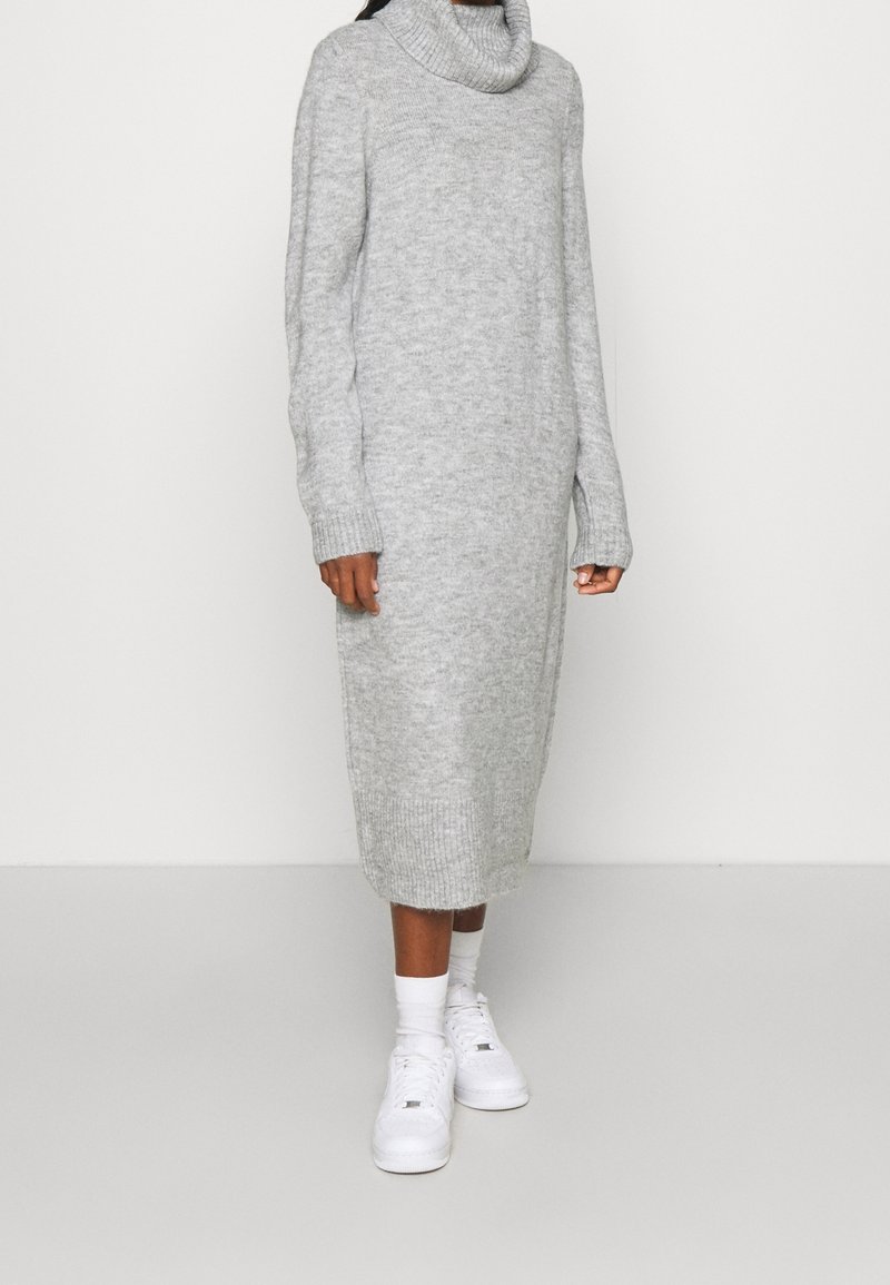 Vestito grigio a collo alto in maglia con maniche lunghe, polsini e orlo a coste; indossato con sneaker bianche, di lunghezza al polpaccio. Texture liscia.