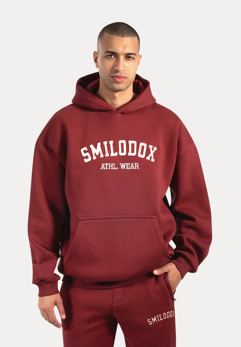 Sudadera burdeos con un bolsillo frontal, logo blanco "SMILODOX ATHL WEAR", puños y dobladillo elásticos, fabricada con suave tejido de mezcla de algodón.