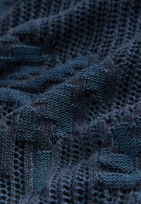 Mørkeblå strikket stof med et tekstureret geometrisk mønster, der indeholder åbent væv og hævede masker.