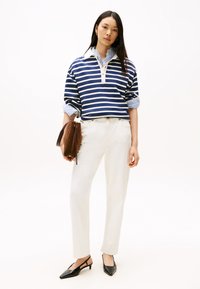 Pullover a righe blu navy e bianche con colletto, abbinato a pantaloni crema e scarpe slingback nere. Il modello tiene una borsa marrone.