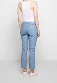 Pantaloni slim-fit di colore blu chiaro realizzati in tessuto morbido, dotati di tasche posteriori e cuciture sottili, indossati con una canotta bianca e sneaker bianche.