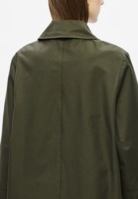 Casaco leve verde-oliva com grande gola, textura suave e costura traseira limpa. Design simples sem ferragens visíveis.