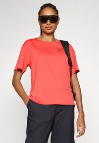Coral short-sleeve t-shirt in lightweight fabric, featuring a crew neckline and a small logo. Worn with black cargo shorts and sunglasses.
